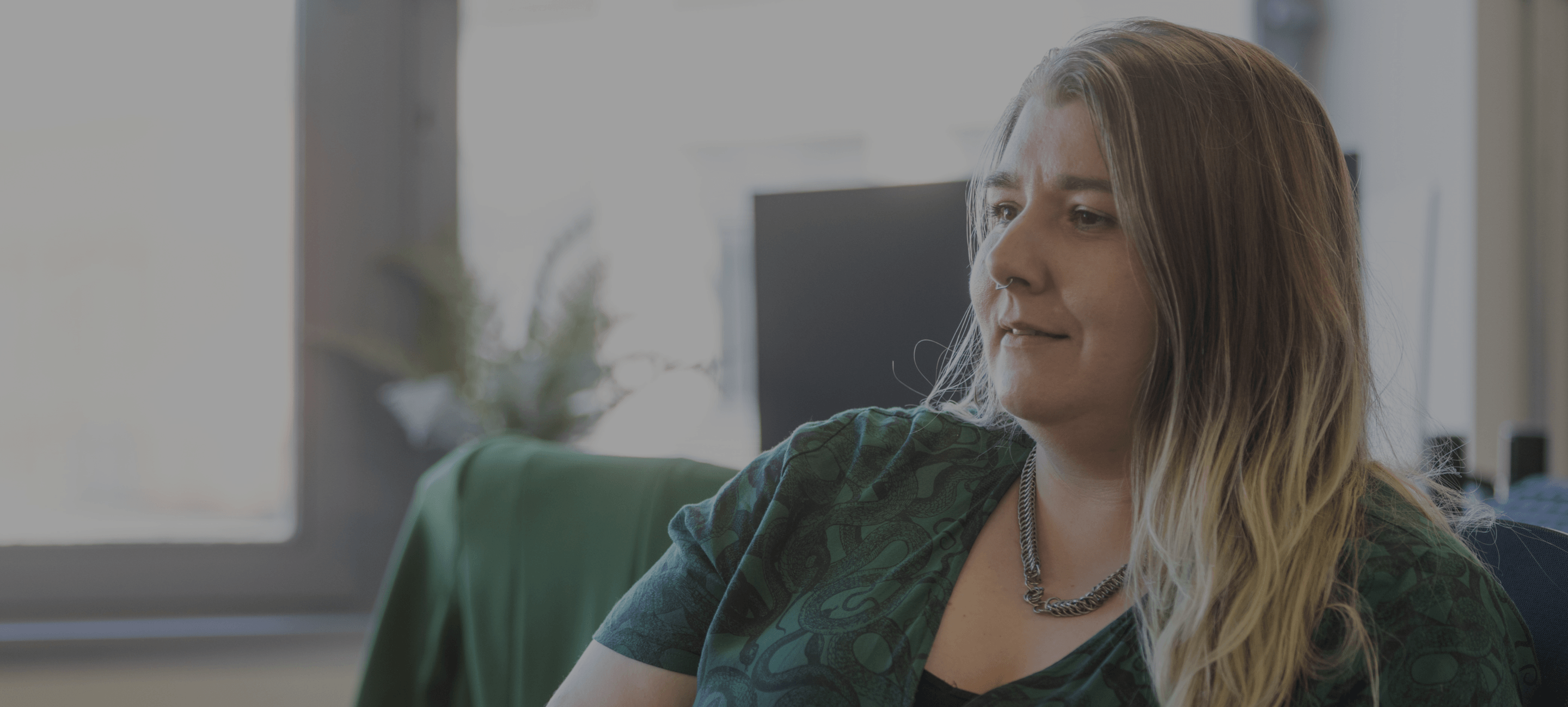 A white woman in a green dress sitting in an office with a dark overlay.