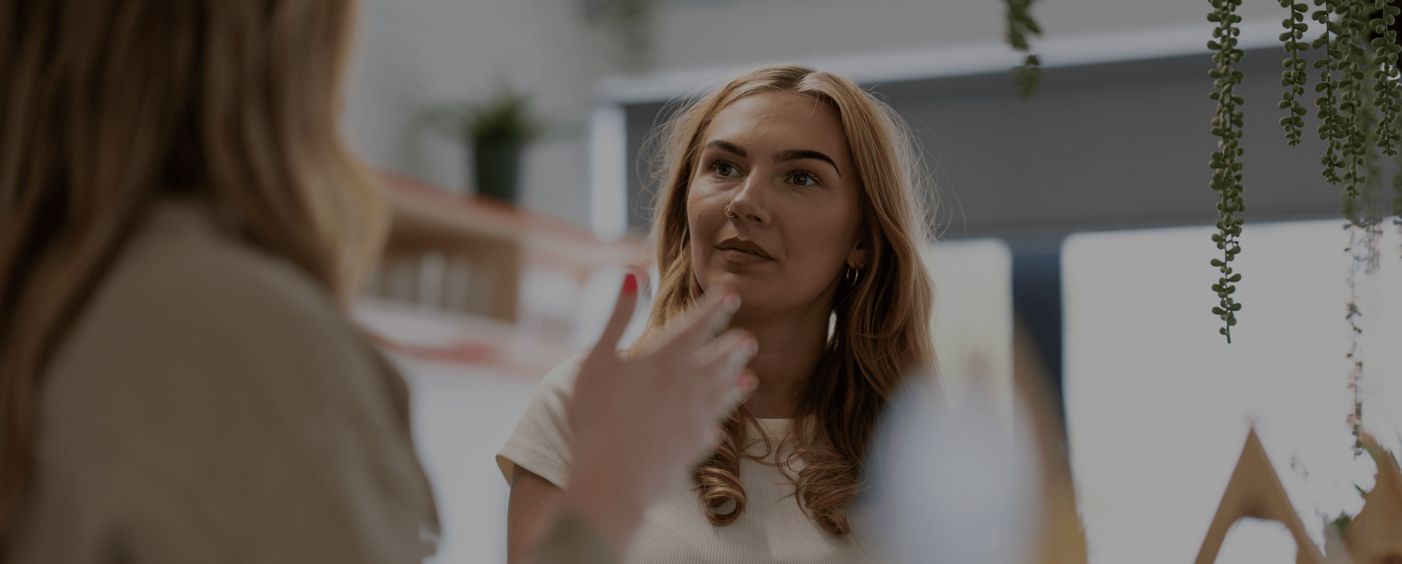 A blonde woman talking to another person with a dark overlay.