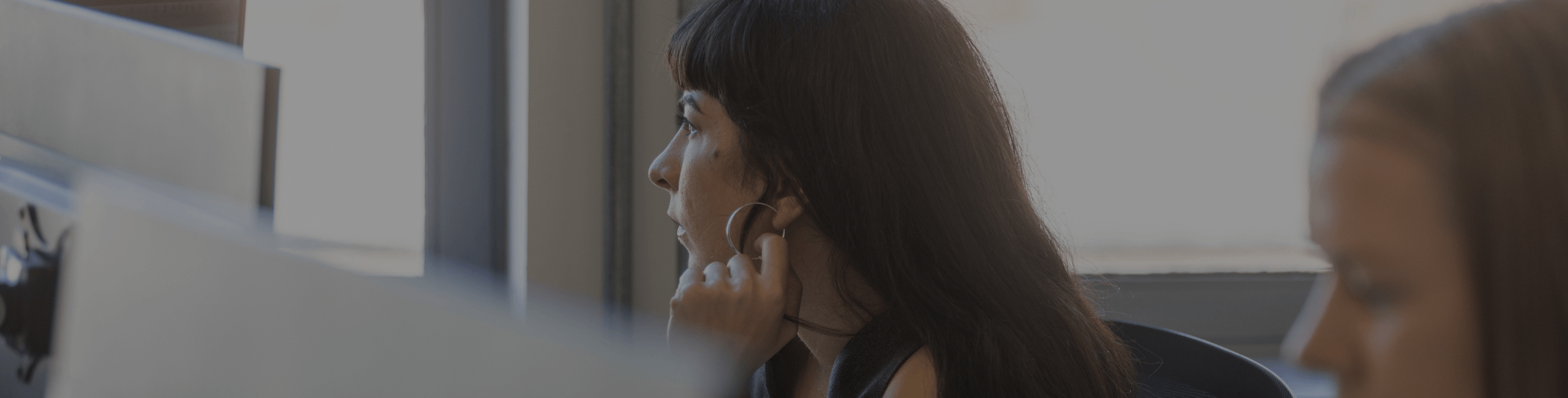 A woman with dark hair sitting at a computer with a dark overlay.